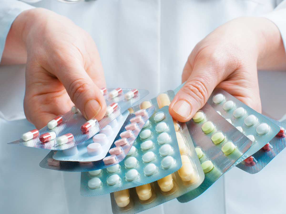 Person in weißem Kittel hält mehrere Blister mit Pillen und Tabletten in den Händen