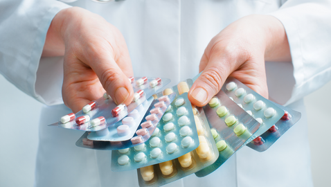 Person in weißem Kittel hält mehrere Blister mit Pillen und Tabletten in den Händen. 